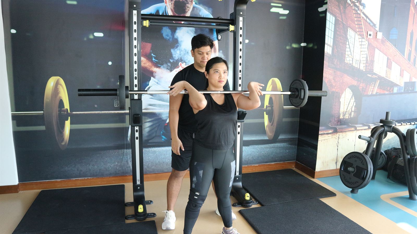 An ATHLI member pressing a barbell overhead with a coach spotting